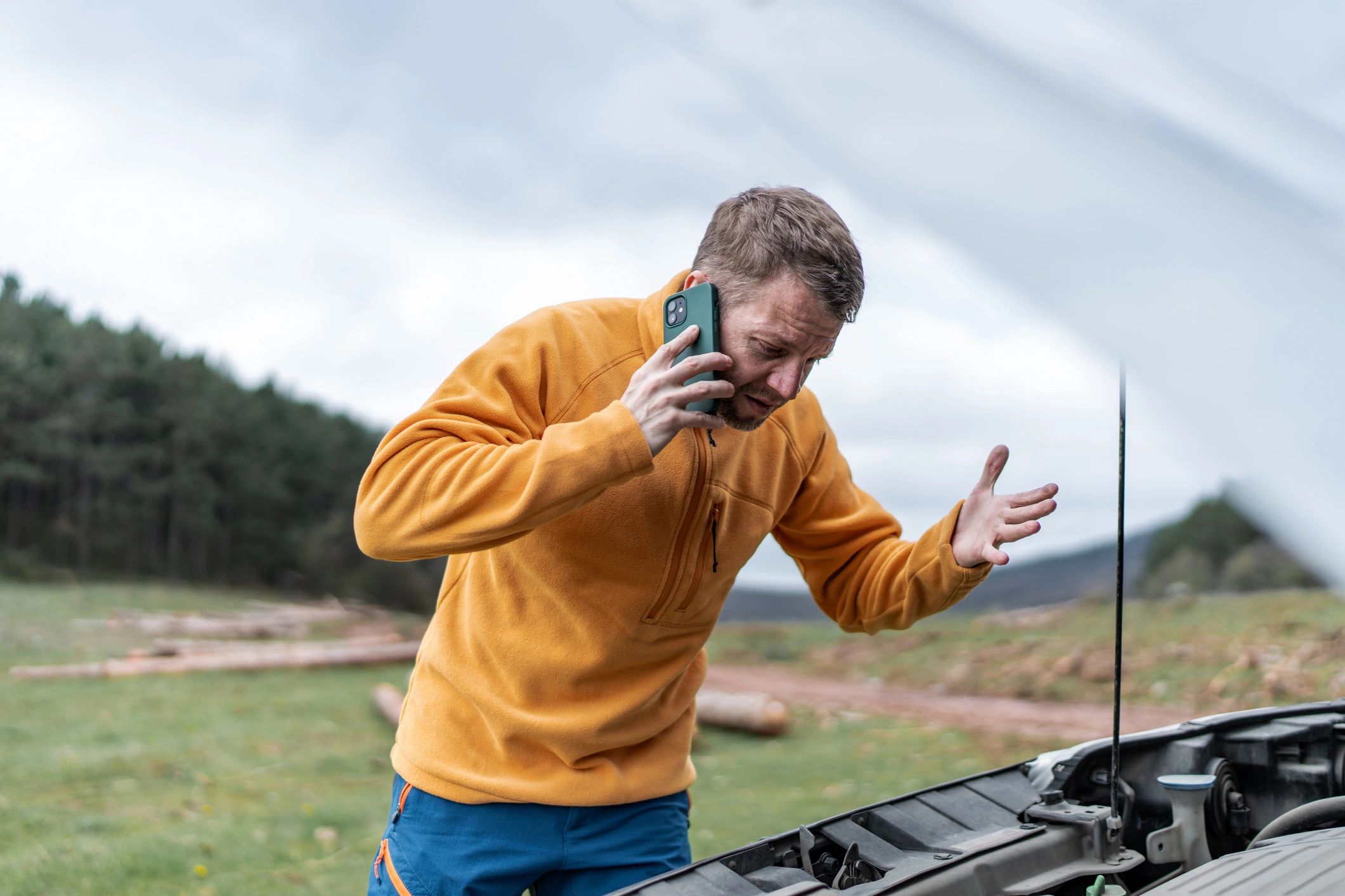 Driver calling for roadside assistance beside a broken down car